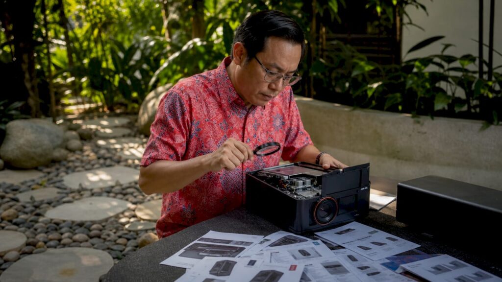 Malaysian man inspecting projector closely at desk