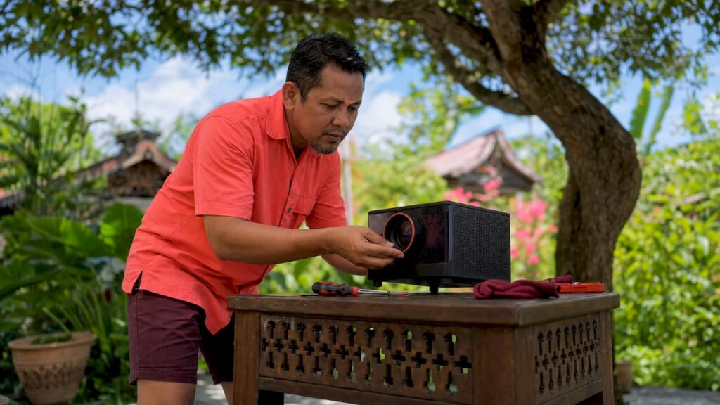 Seorang lelaki sedang memeriksa lensa projektor di ruang tamu rumahnya.